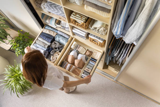 A person organizes a neatly arranged wardrobe drawer full of minimalist, color-coordinated clothing.