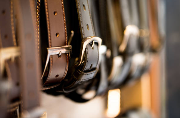 Close-up of various leather belts hanging in a row, illustrating timeless and simple accessory choices.